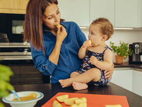 Mamá y bebé comiendo fruta en la cocina.