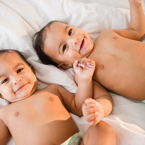 Bebés gemelos sonriendo acostados en la cama.