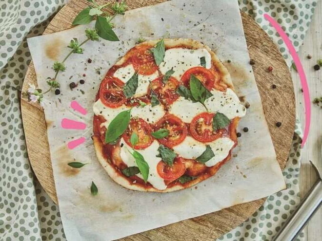 Pizza margarita en el centro con decoración de queso y albahaca alrededor