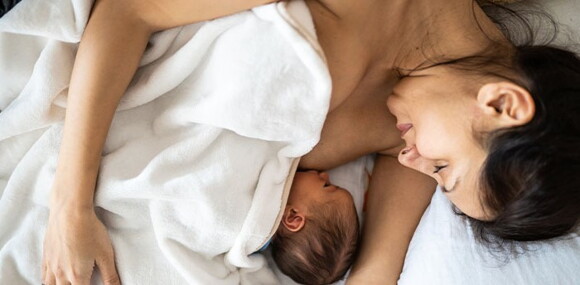 Mamá acostada alimentando a su bebé recién nacido.