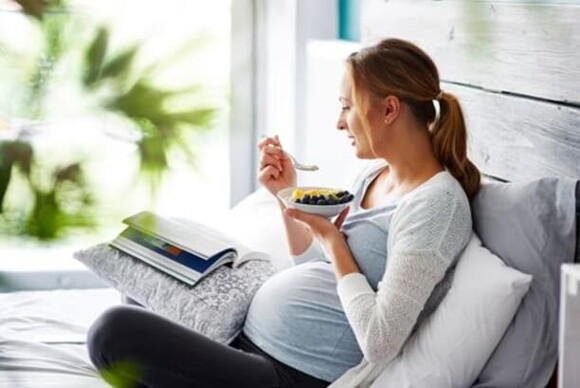 Mujer embarazada sentada comiendo frutas.