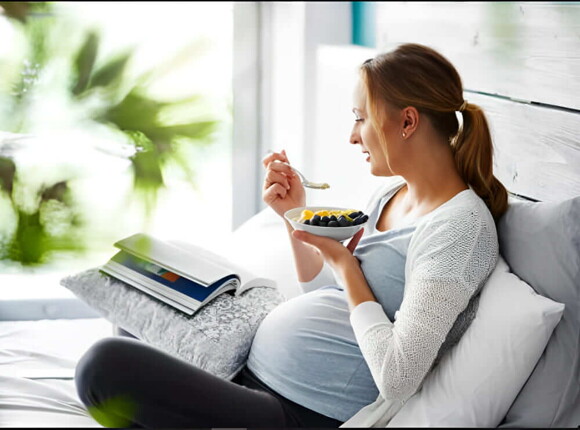 Mujer embarazada comiendo mientras lee un libro