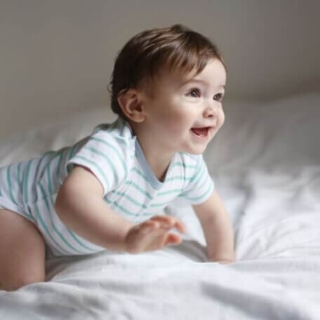 Niño sonriendo y gateando como parte del desarrollo psicomotor.